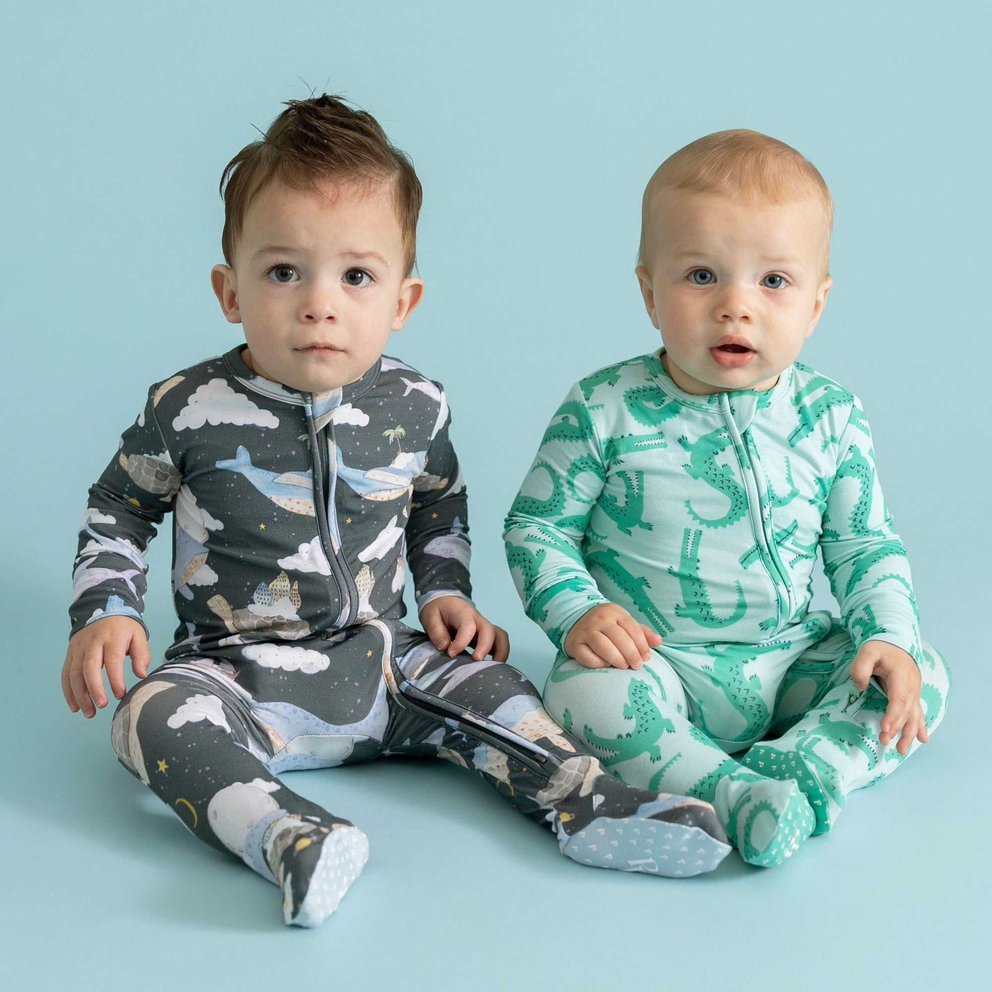 two toddler boys sitting wearing animal themed print one piece bodysuits