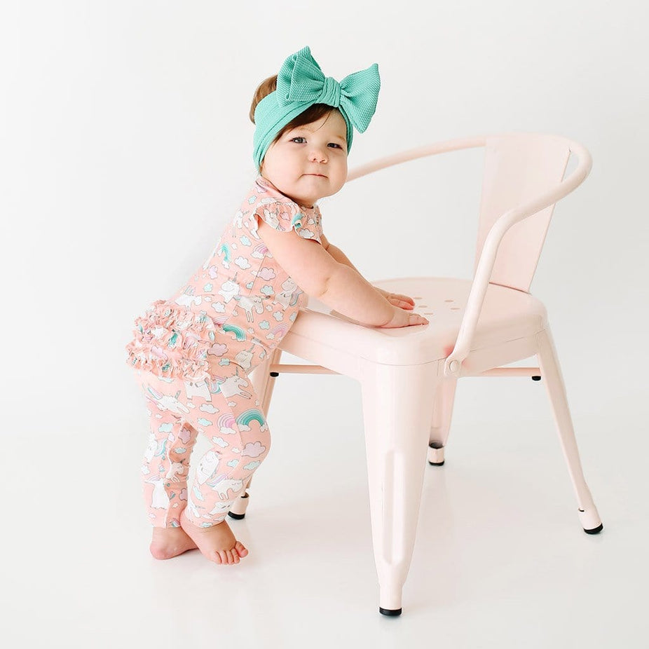 Standing baby wearing pink Olive Ruffled Cap Sleeve Romper with unicorn pattern