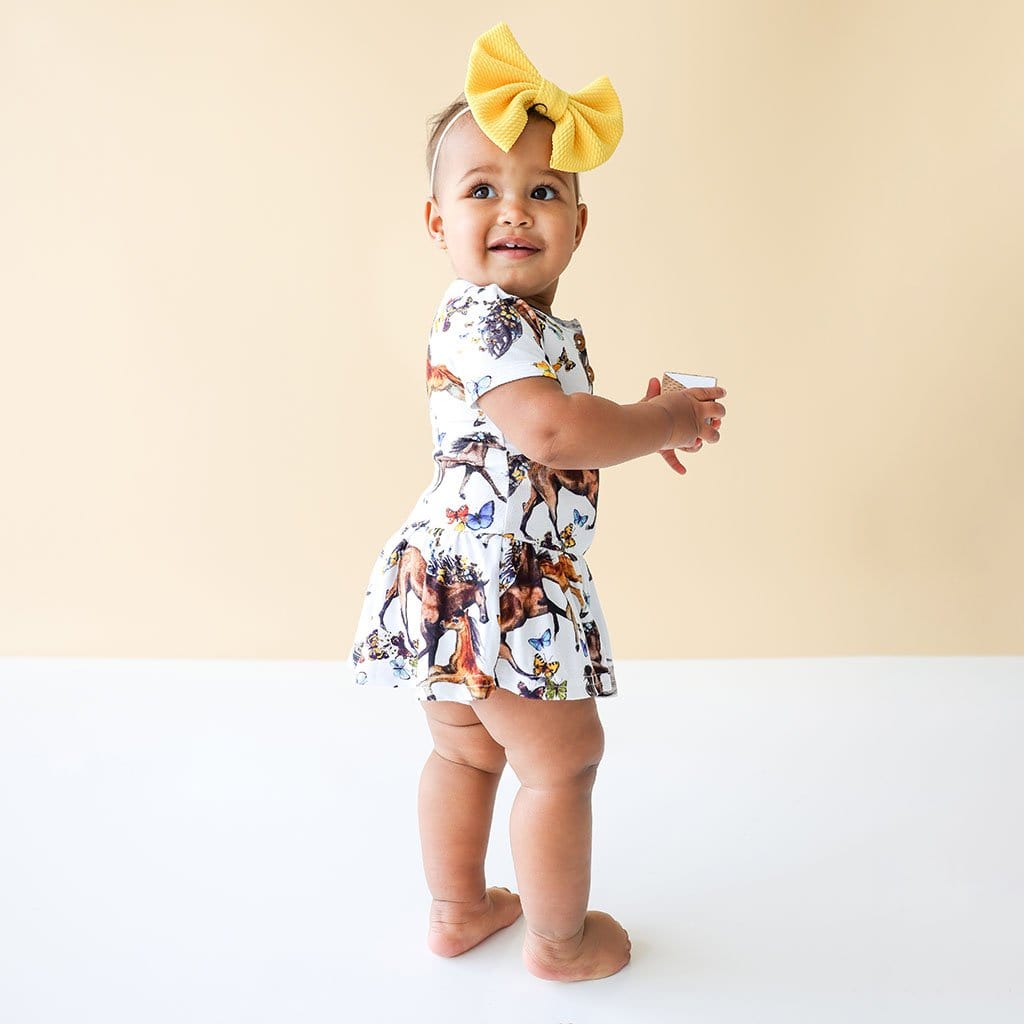 Baby in yellow ribbon wearing Claire Short Sleeve Henley Twirl Skirt Bodysuit in animal print