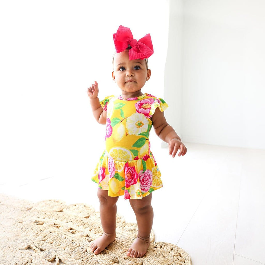Baby in red ribbon wearing Annika Ruffled Cap Sleeve Twirl Skirt Bodysuit