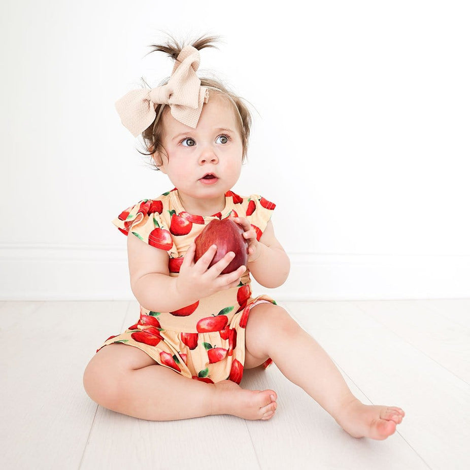 Baby holding an apple wearing Finn Ruffled Cap Sleeve Henley Twirl Skirt Bodysuit