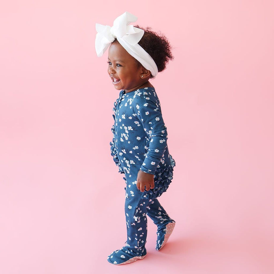 Baby girl in blue floral long sleeve onesie footies and a white headband.bow
