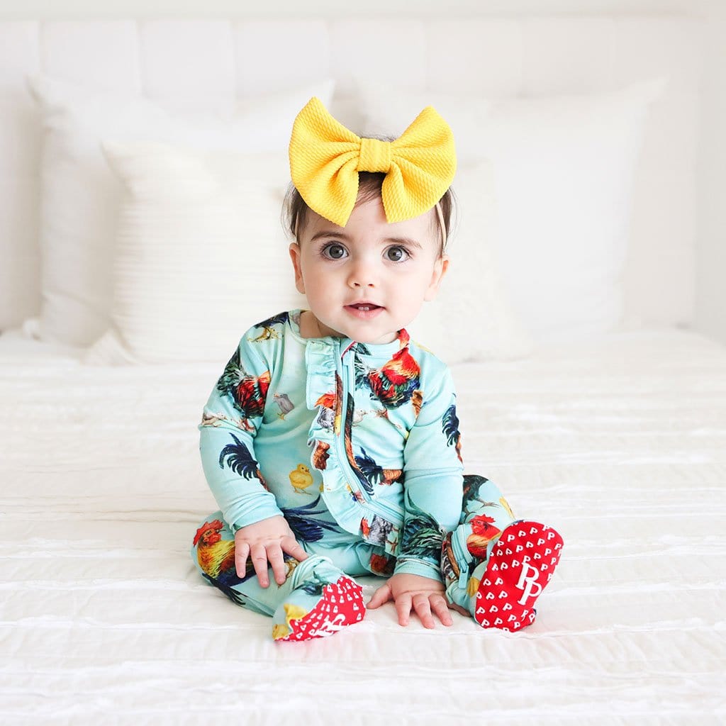 Baby in yellow ribbon wearing Rhett Footie Ruffled Zippered One Piece