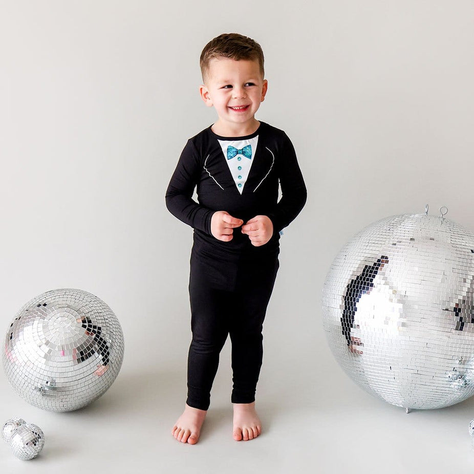 Toddler Boy in Tuxedo Toddler Pajamas with New Year's Eve Balls Behind Him
