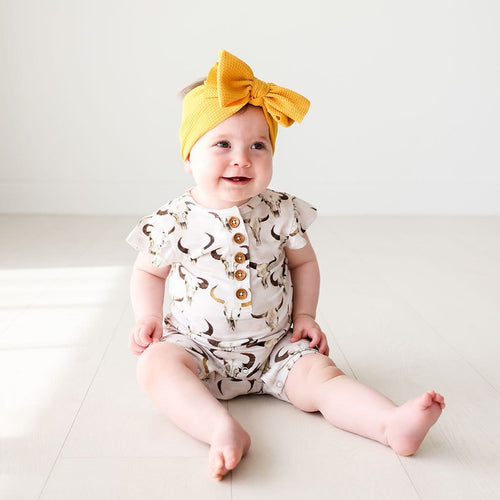 Baby in yellow ribbon wearing Austin Ruffled Cap Sleeve Henley Short Romper