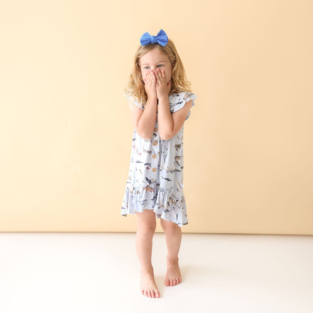 Toddler in blue ribbon wearing Maverick Ruffled Cap Sleeve Henley Hi-Low Dress